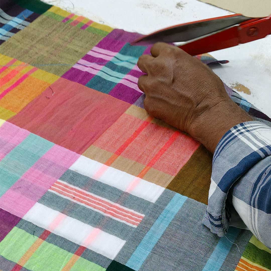 close up on a mans hands cutting a colorful plaid fabric with scissors